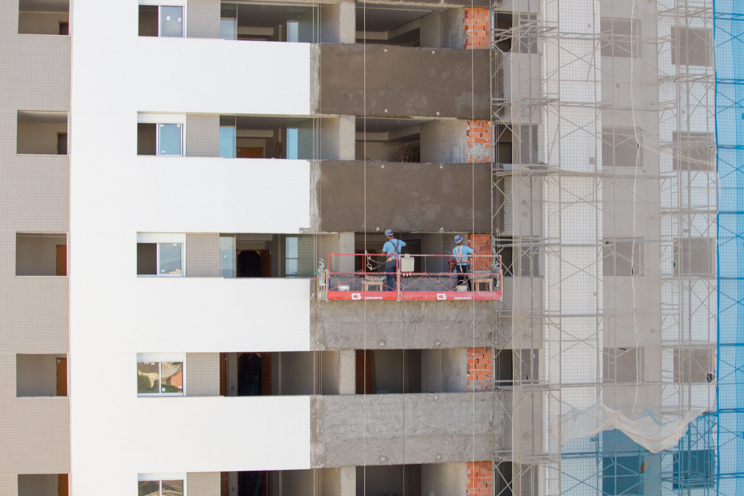 Imagem da fachada de uma obra de edifício residencial Empominas, com trabalhadores em um andaime executando a obra.