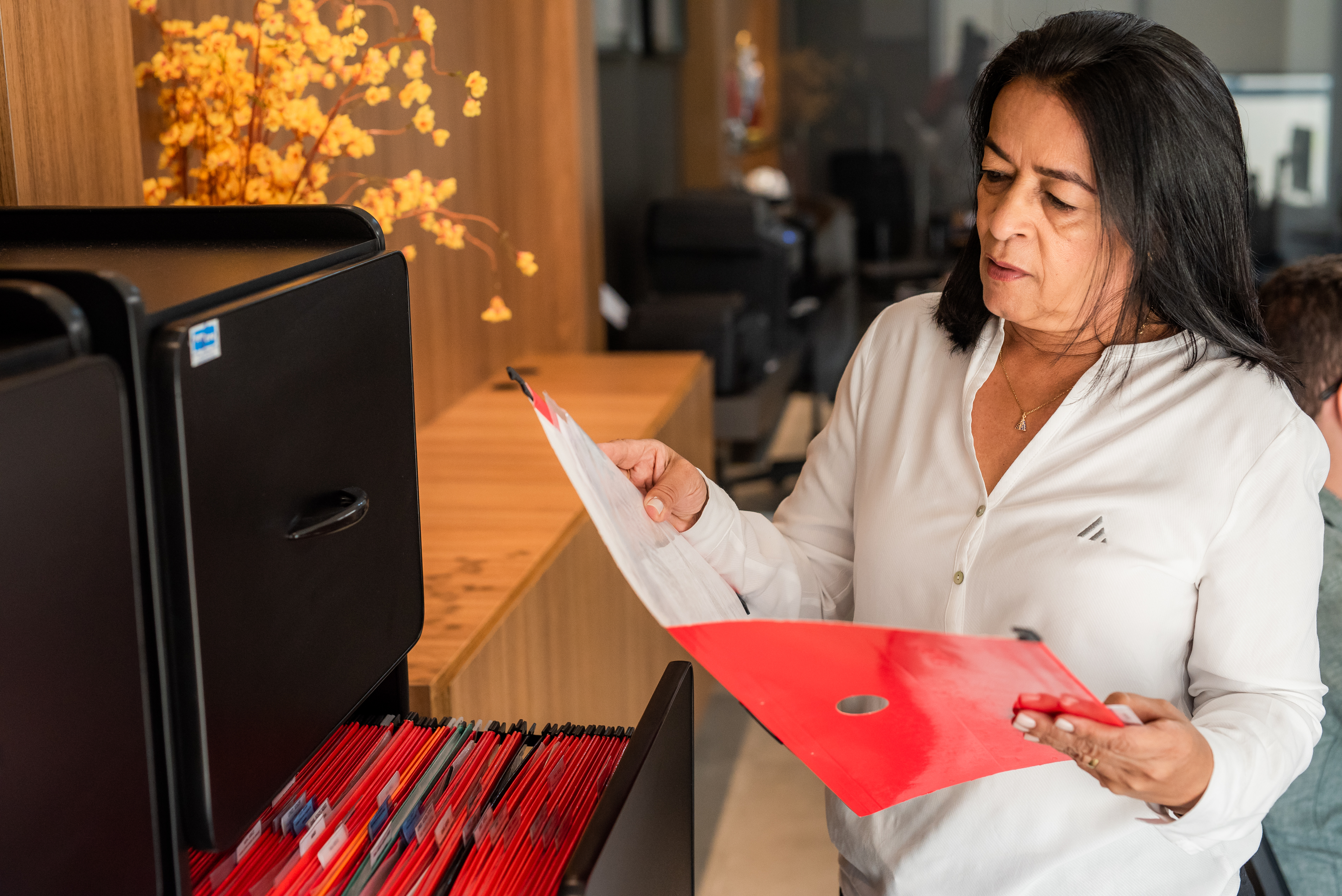 Funcionária Empominas lendo documento em uma pasta de papel, no escritório da empresa.